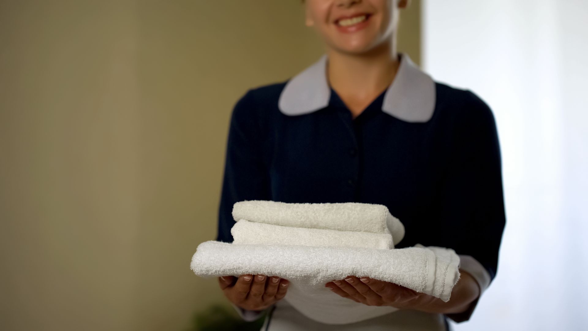 Smiling hotel worker showing clean pillows, good housekeeping, health standard